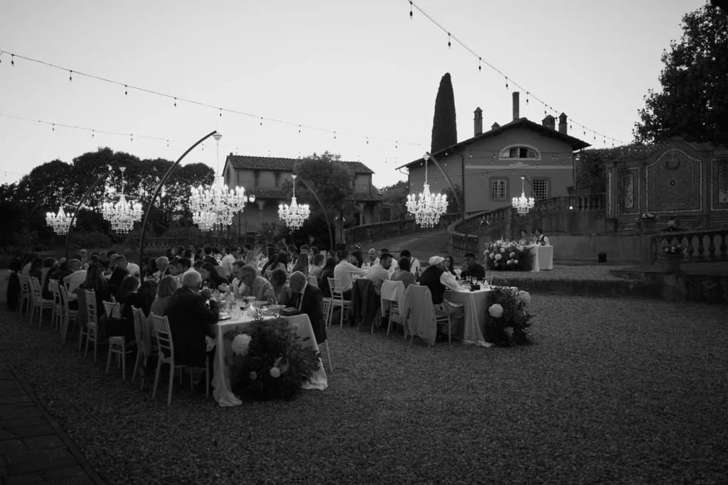 Cena di matrimonio in Toscana nel giardino della villa al tramonto, tavoli imperiali con lampadari chandelier