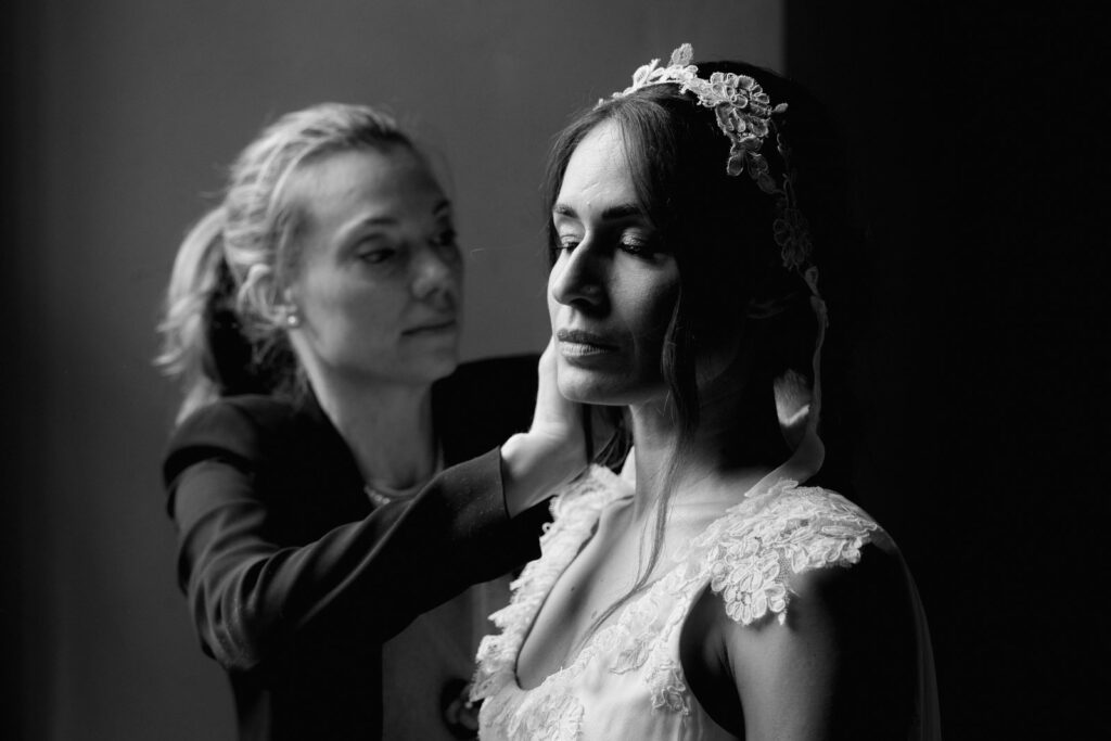 Sposa con velo in pizzo aiutata da una donna durante la vestizione, foto in bianco e nero