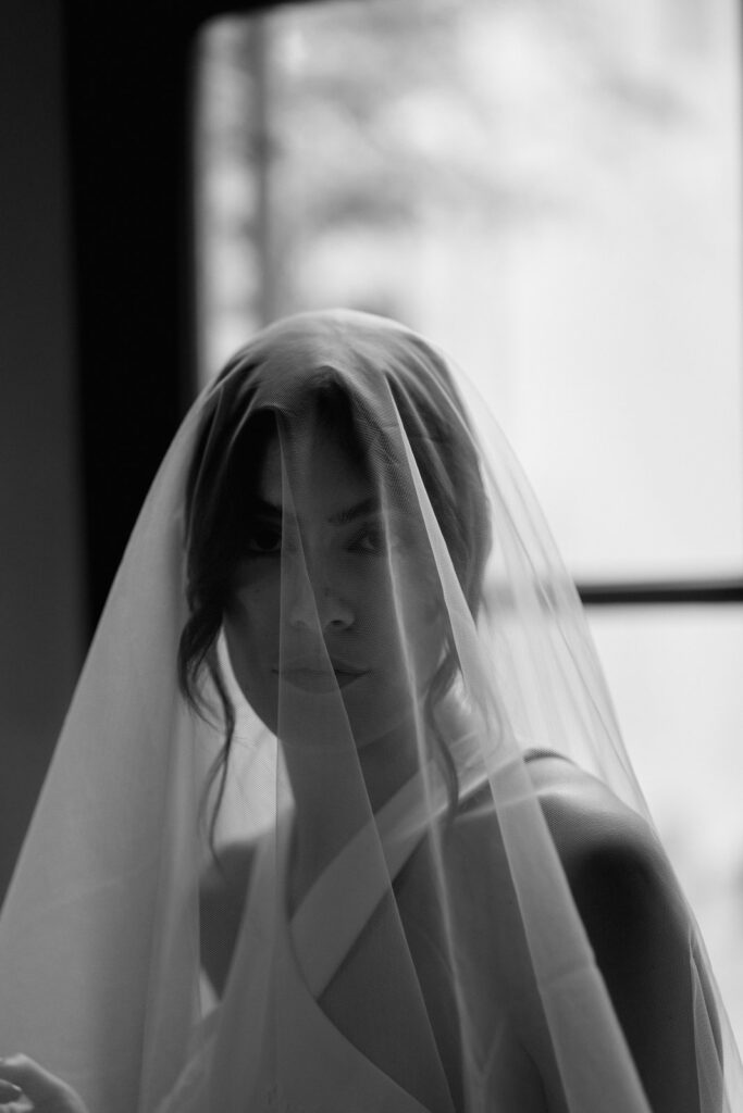 Sposa con velo di tulle sul viso in controluce durante la prova dell'abito da sposa